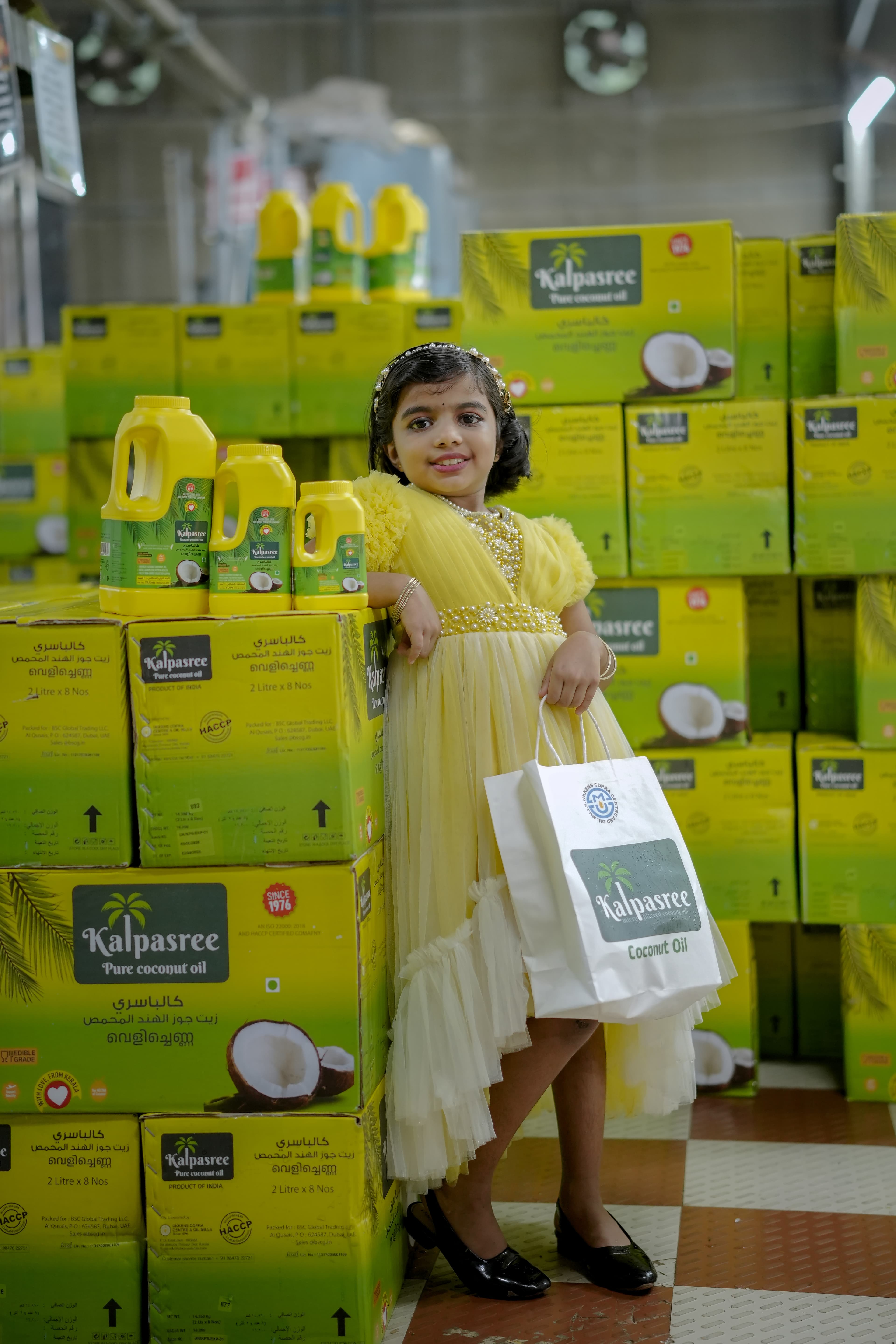 A child beside pallets of Kalpasree coconut oil cartons ready for export